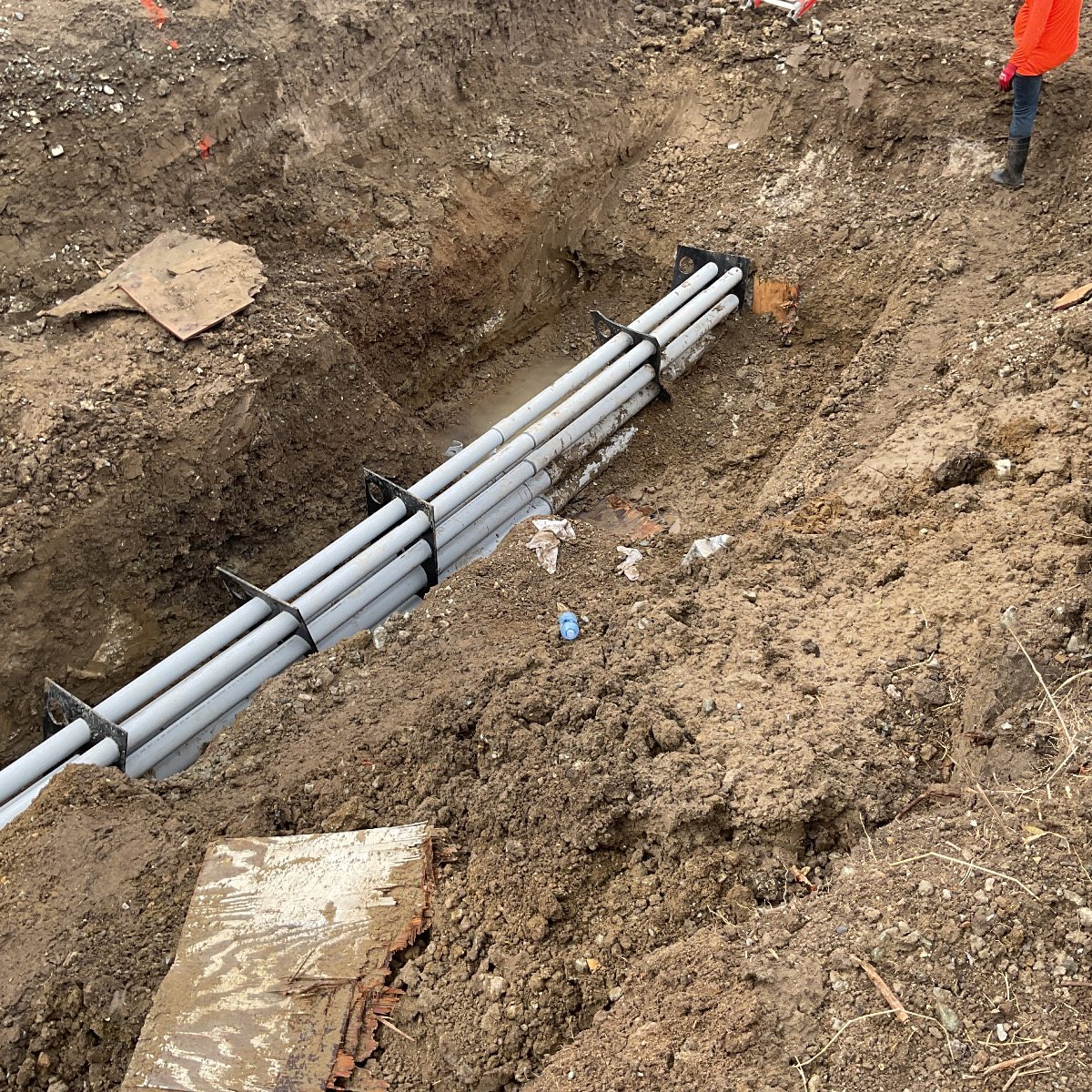 Bundled PVC conduit held on spacers in an open trench, forming a duct bank.