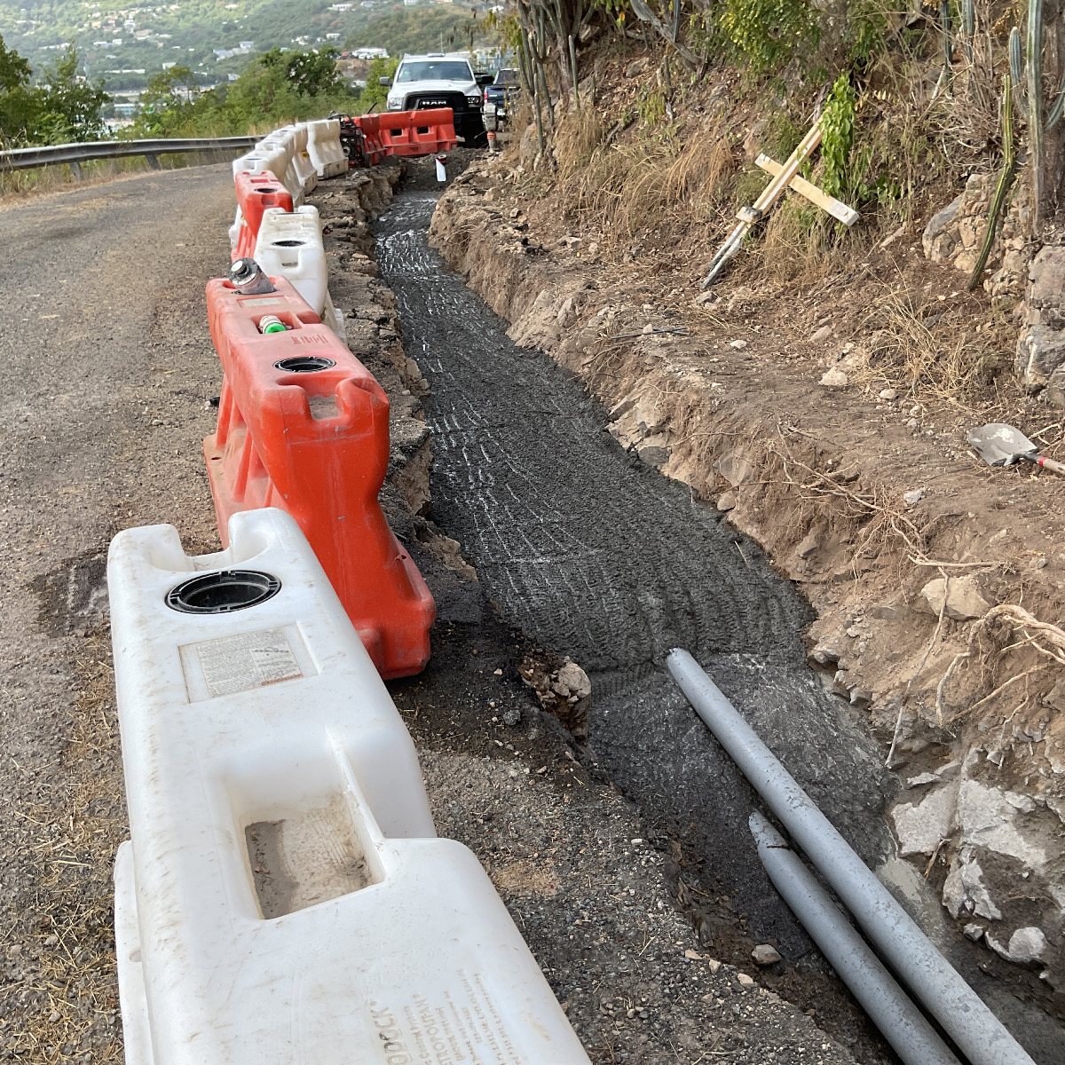A concrete-encased duct bank running along the edge of a hillside road.