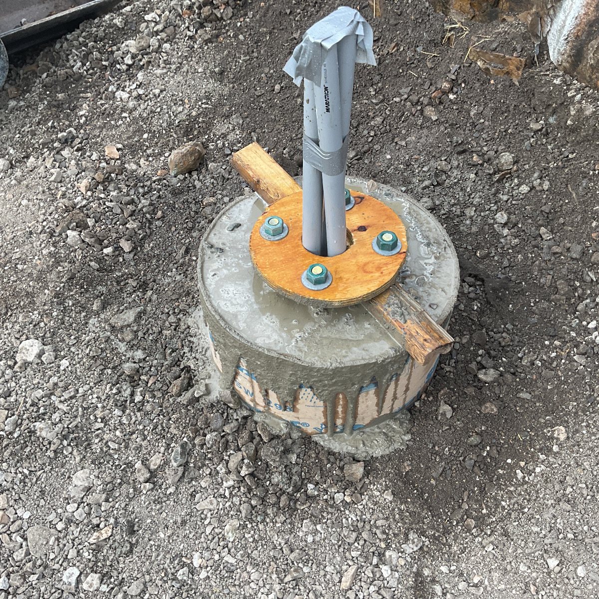 A cured concrete pier with an anchor-bolt template and conduit stub.
