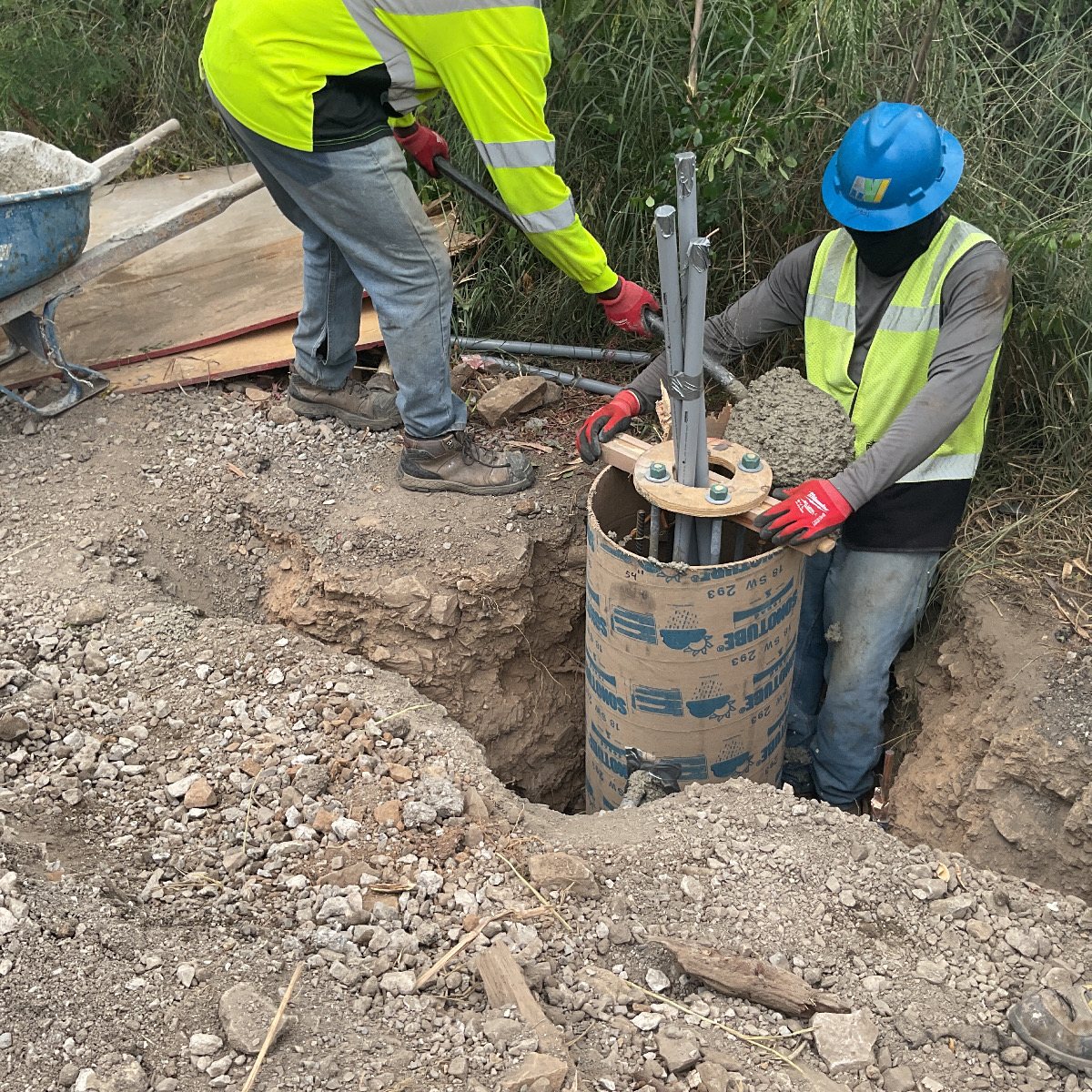Two workers setting a pole foundation with an anchor-bolt template and conduit.