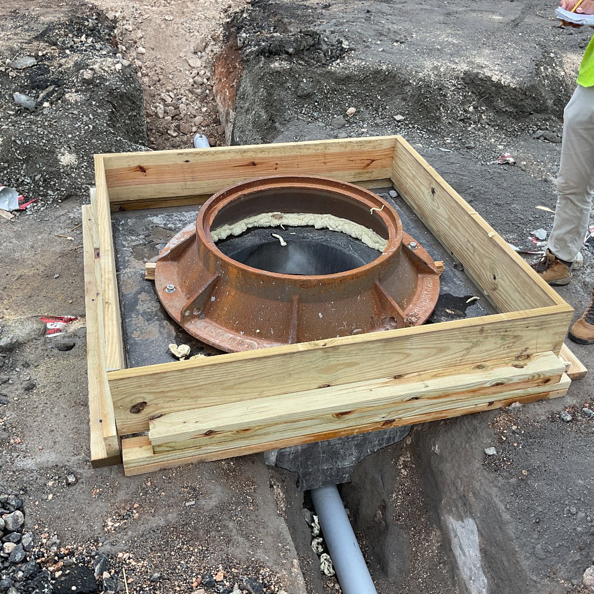 A manhole frame boxed in wood formwork and sealed, ready for concrete.