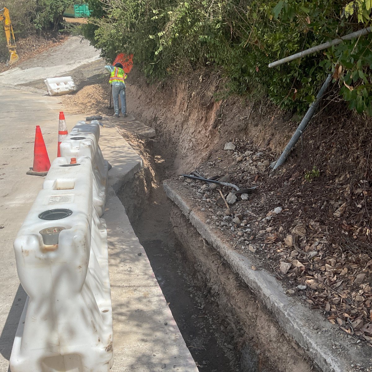 A worker and traffic control along an active roadside trench.